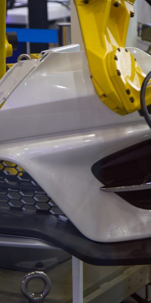 A yellow robotic arm uses a 3D laser scanner for quality control on a composite car bumper, a key process for collecting the physical data needed for composite simulation validation.