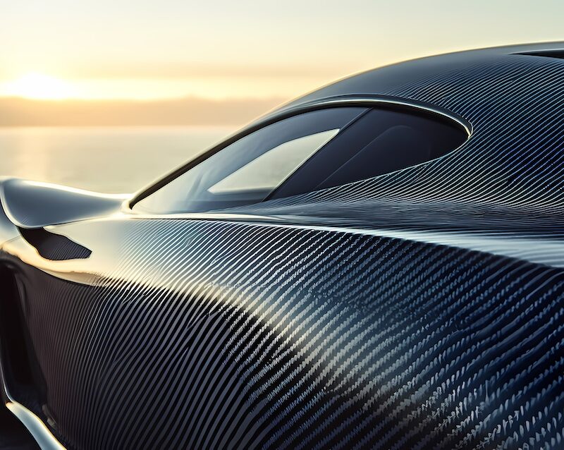 A close-up of a Koenigsegg Regera's exposed carbon fiber body, showing the intricate V-pattern weave of the advanced composite material at sunset.